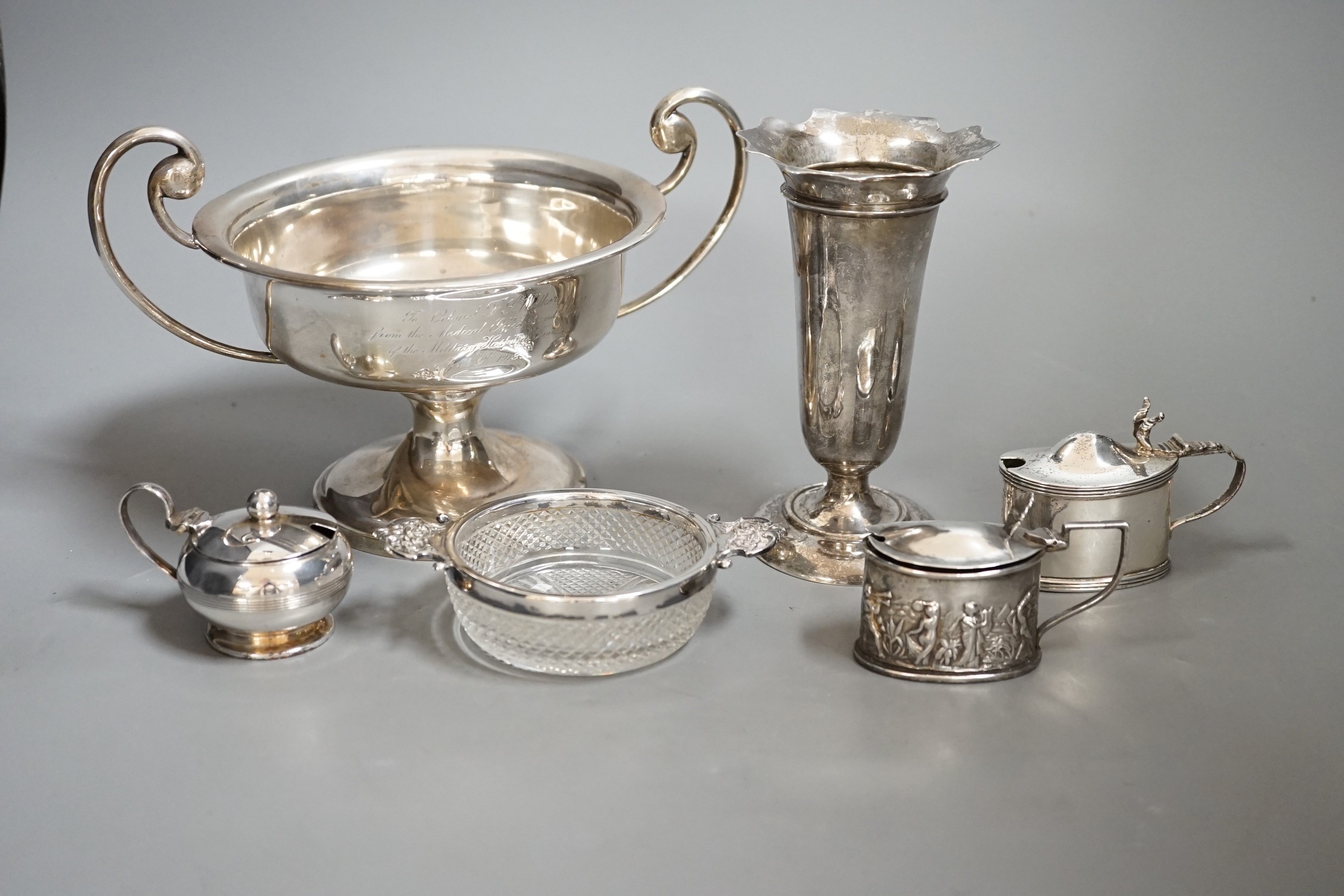 A group of assorted small silver items to include a posy vase, silver-mounted cut glass quaich, a twin-handled silver cup and three condiments.